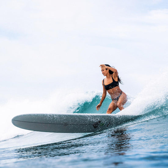 Kelia surfing on a long white surf board.