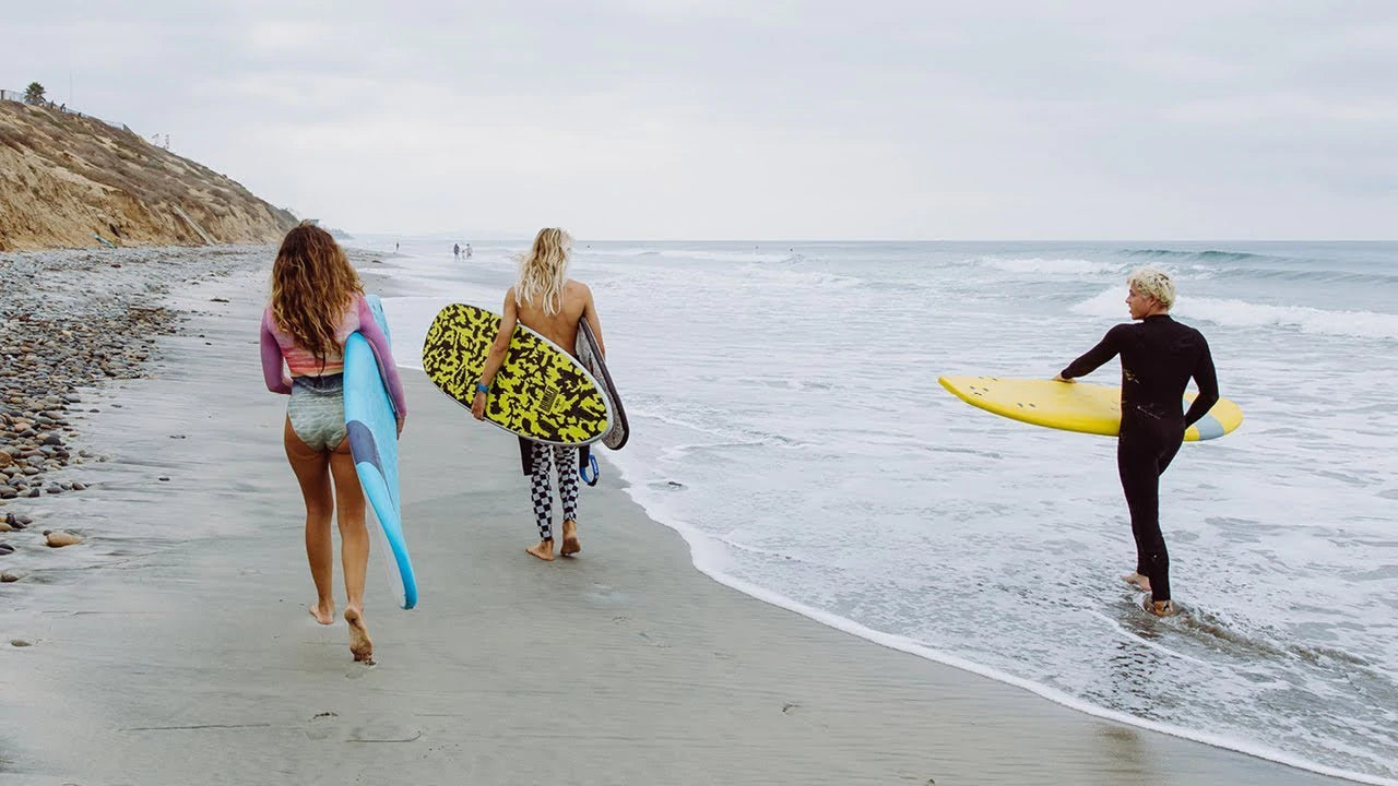 Three surfers walk along the beach, holding their surf boards.